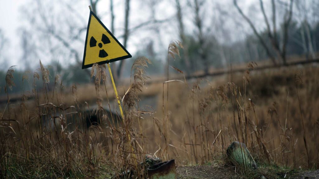Ein Strahlenwarnzeichen steht in der Sperrzone um das explodierte Atomkraftwerk Tschernobyl auf einem Feld.