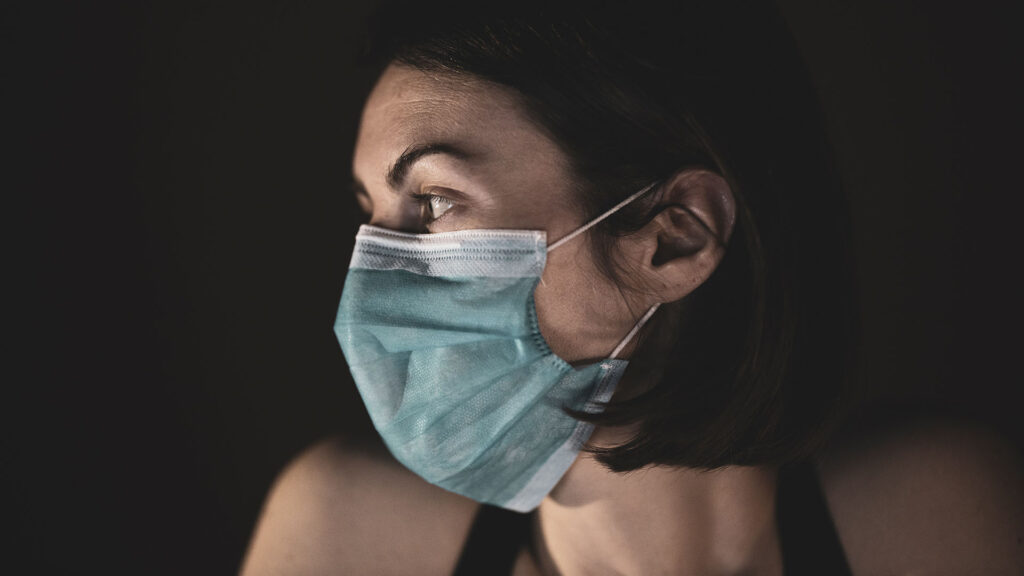Dunkelhaarige Frau mit Maske im Profil.