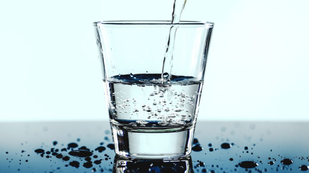 Ein Glas das auf einem Tisch steht und in das Wasser eingeschüttet wird.