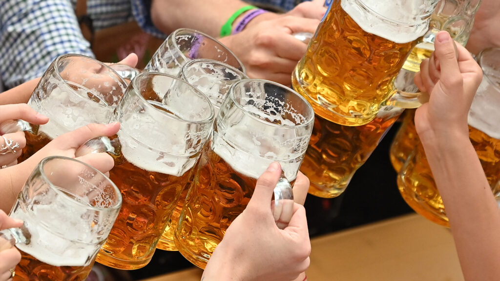 Oktoberfest 2023. Volles Festzelt. Besucher feiern und prosten sich mit Bierkrügen zu.