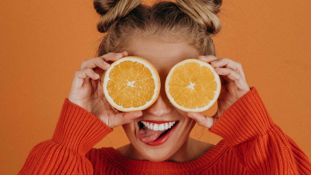 Mädchen hält sich lachend zwei Orangenhälften vor die Augen.