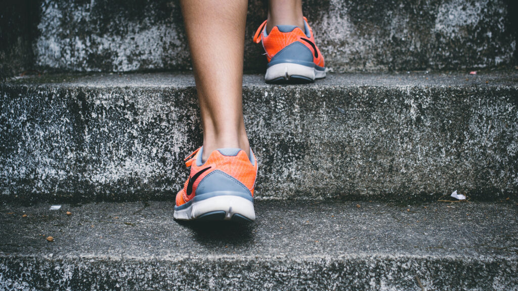 Person mit orangefarbenen und grauen Schuhe, die auf grauer Betontreppe geht