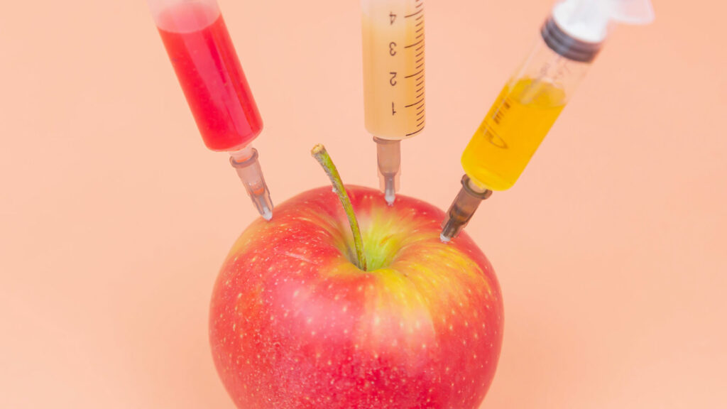 Drei Spritzen stecken in einem Apfel.