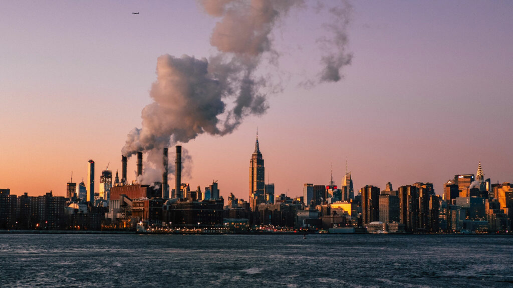 Die New Yorker Skyline bei Sonnenuntergang. Zu erkennen sind viele Abgase die in den Himmel aufsteigen.
