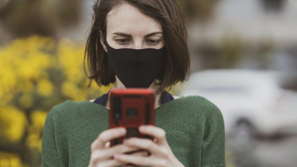 Eine Frau mit Mund-Nasen-Schutz schaut auf ihr Handy.