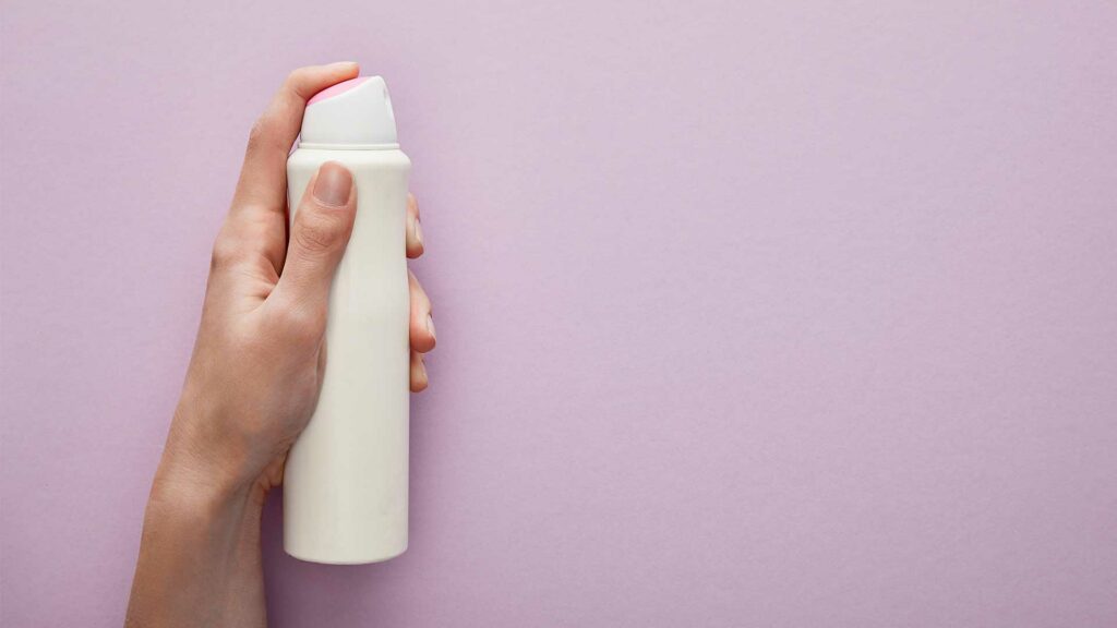 Nahaufnahme einer Hand die eine weiße Deodose hält.