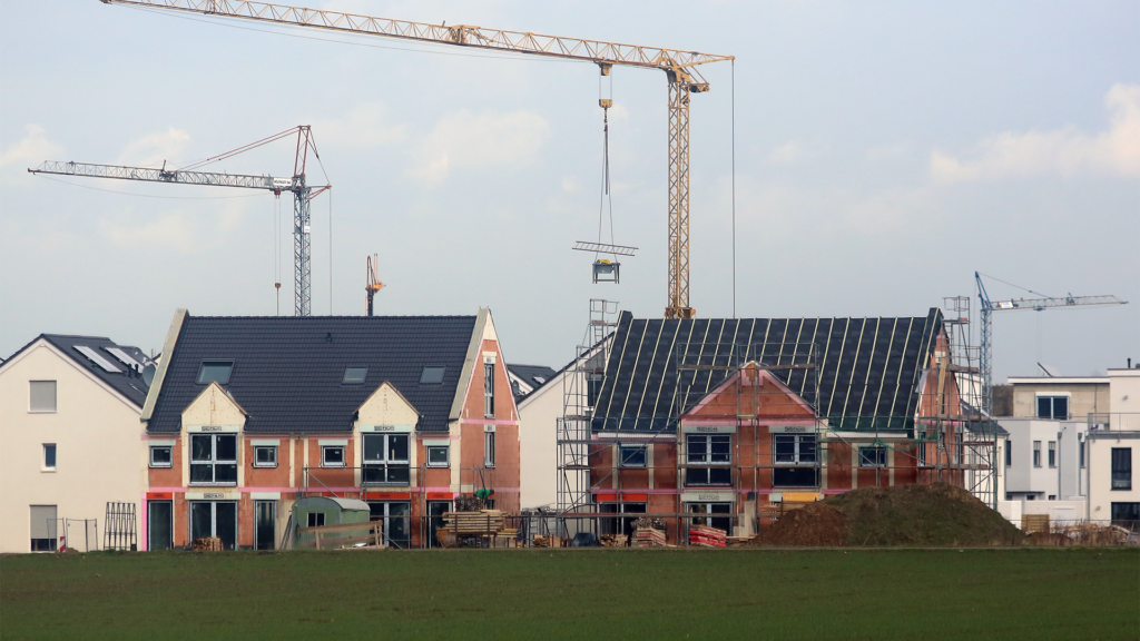 Mehrere Einfamilienhäuser im Bau, mit Kränen und Gerüsten in einem Neubaugebiet.