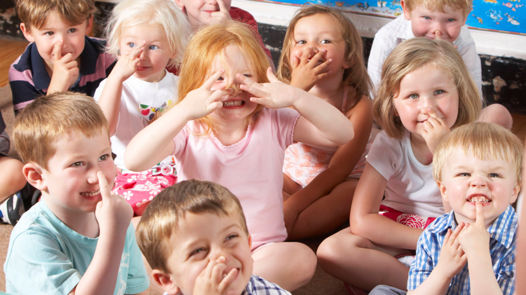 Eine Gruppe von Kindern im Kindergartenalter sitzt auf dem Boden und zieht Grimassen.
