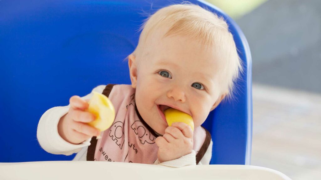 Baby isst im Kinderstuhl einen Apfel.