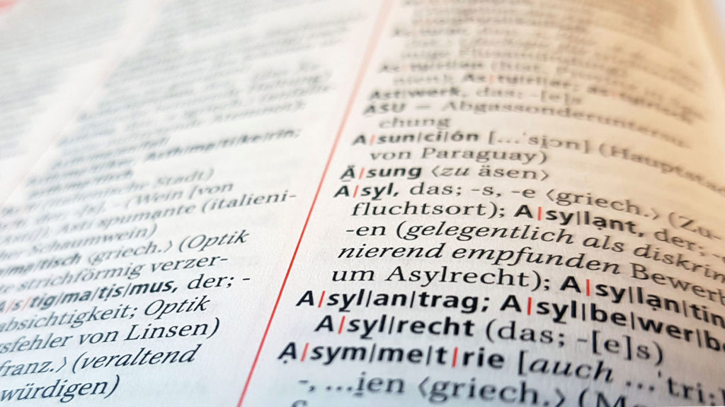 Nahaufnahme einer aufgeschlagenen Wörterbuchseite mit Fokus auf das Wort "Asyl" und seine Silbentrennung.
