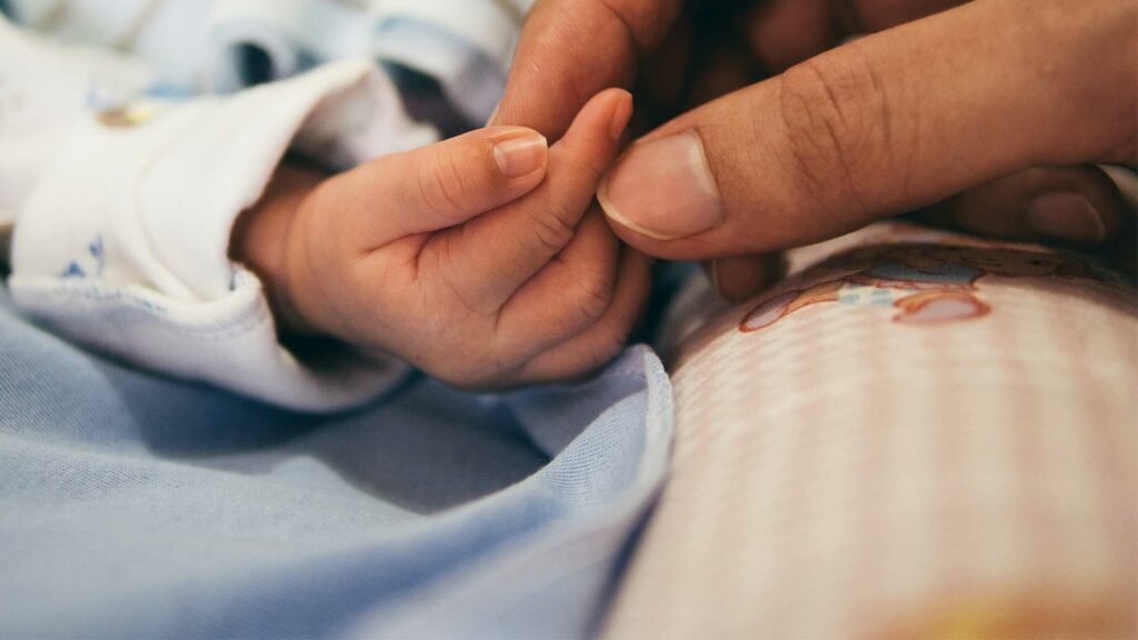 Finger eines neugeborenen Kindes und die einer Mutter berühren sich auf einer Kinderdecke.