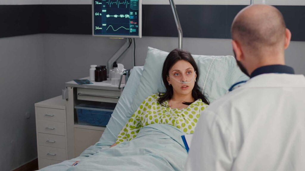 Eine Frau liegt im Krankenhausbett, vor ihr steht ein Arzt, der ihr etwas erzählt