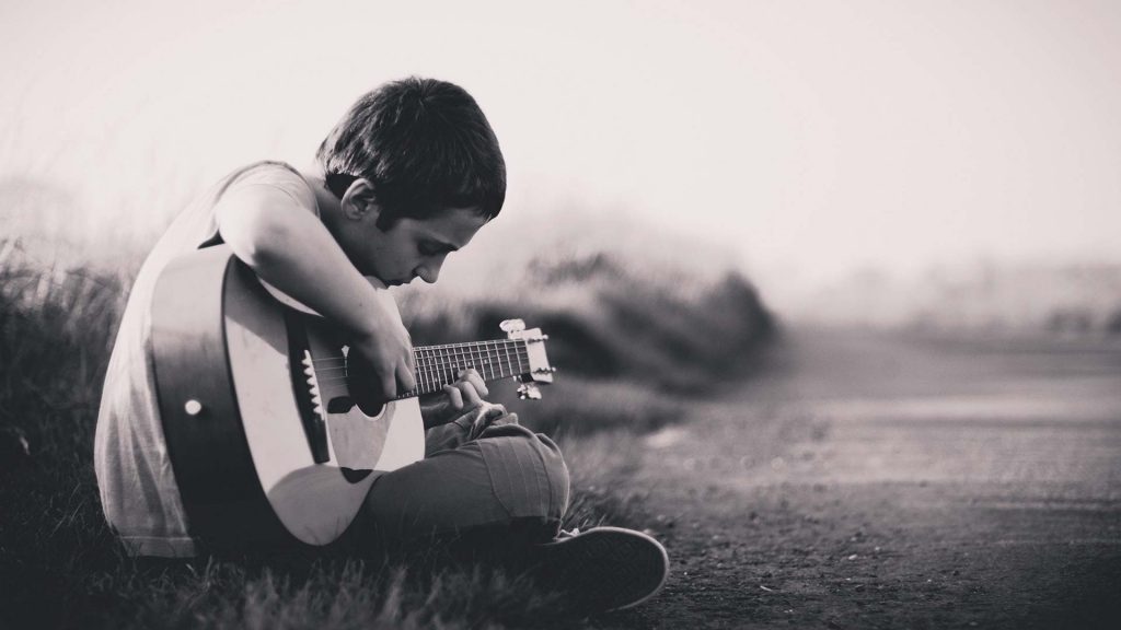 Ein Junge sitzt auf einer Wiese und spielt Gitarre.