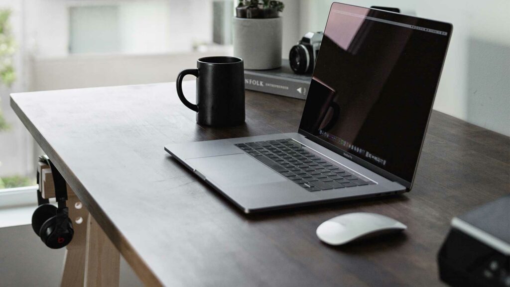 Home Office Schreibtisch am Fenster mit Laptop, Maus, Kaffeetassen und weiteren Büroutensilien. Bild: Dillon Shook/unsplash,