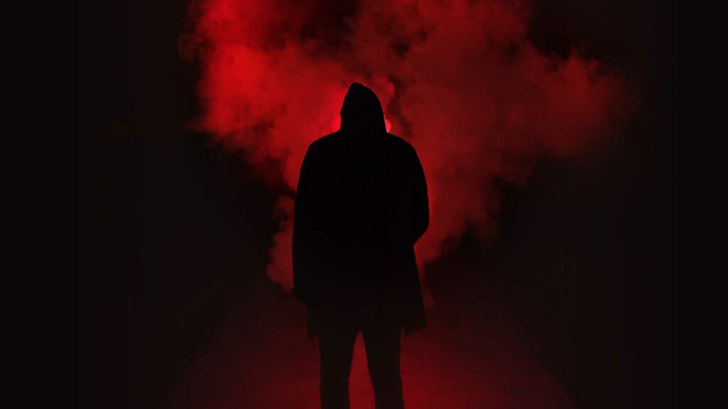 Ein Mann, der bloß anhand einer dunklen Silhouette zu erkennen ist, steht vor rotem Rauch.