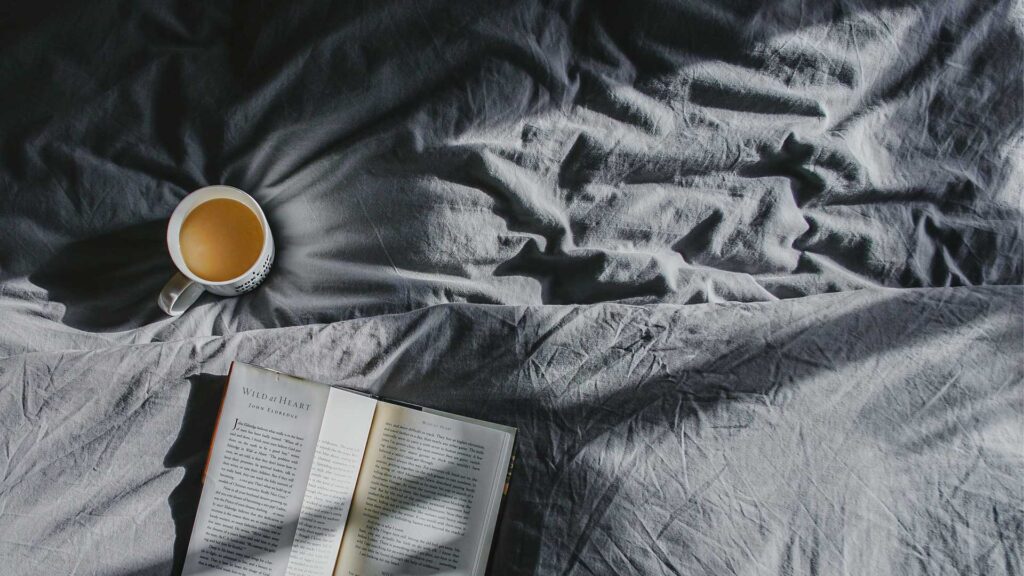Eine volle Kaffeetasse und ein Buch liegen auf einem Bett.