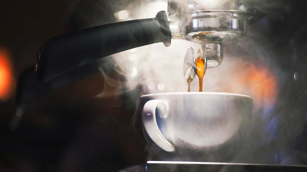 Frischer Kaffee fließt aus einer Siebträgermaschine in eine weiße Tasse.