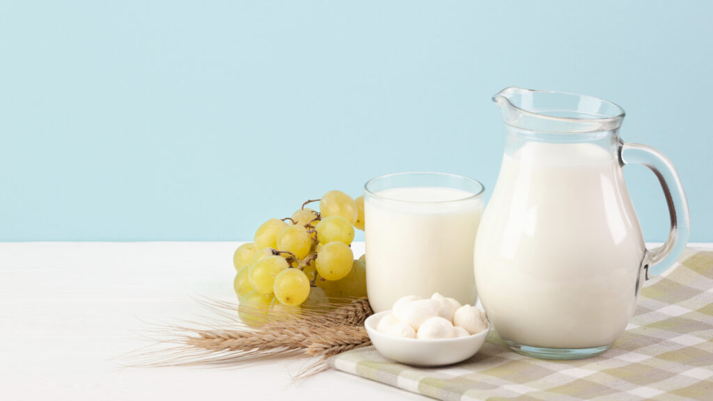 Ein Krug und ein Glas Milch neben Trauben und einer Schale Käse
