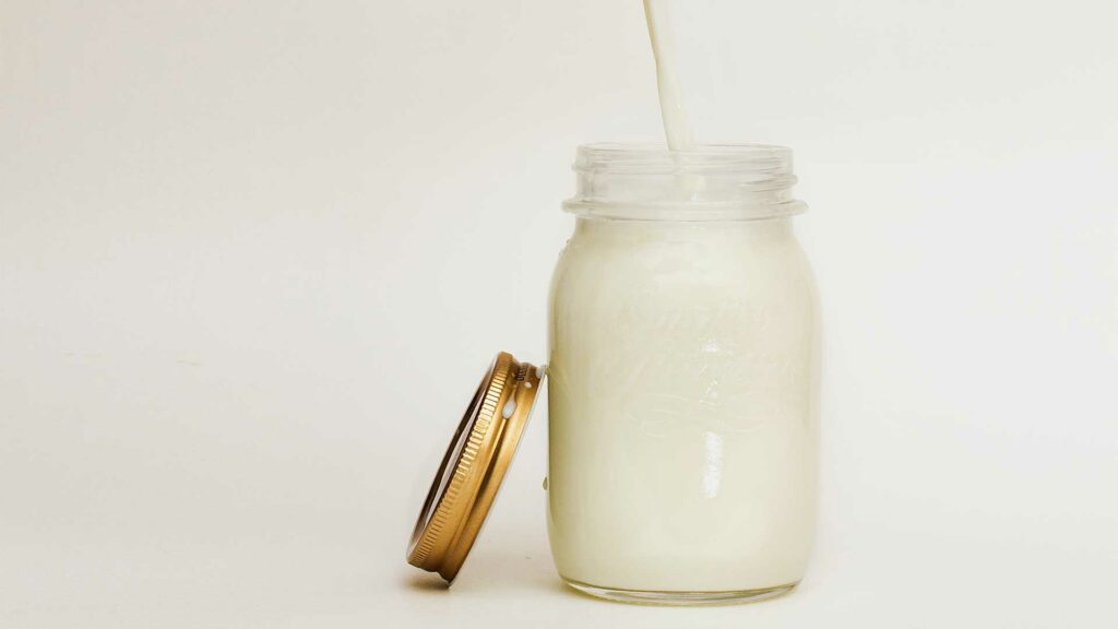 Volles Glas Milch, daneben lehnt ein goldener Deckel.