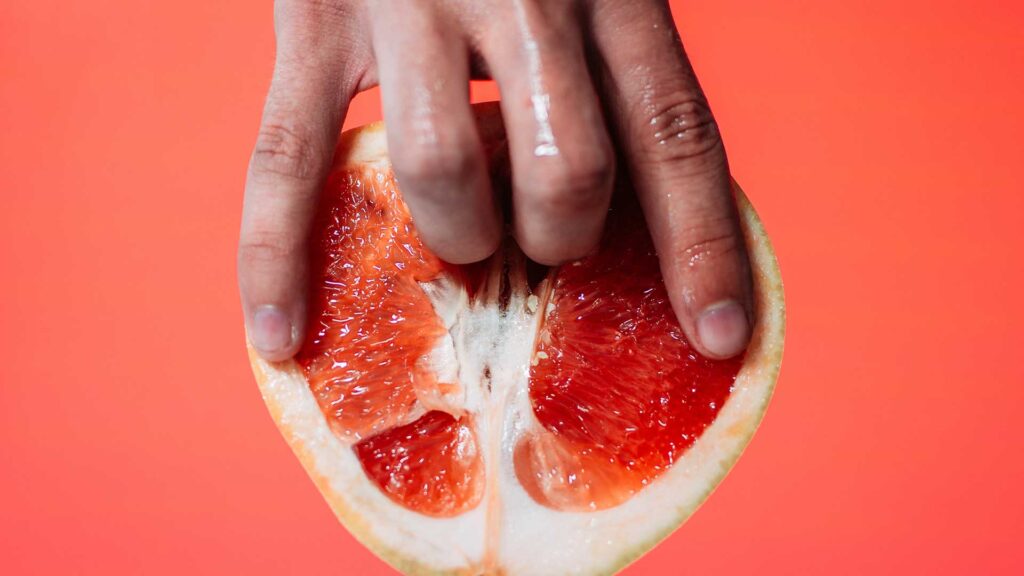 Ein Zeige- und Mittelfinger werden eine halbierte Blutorange eingeführt.