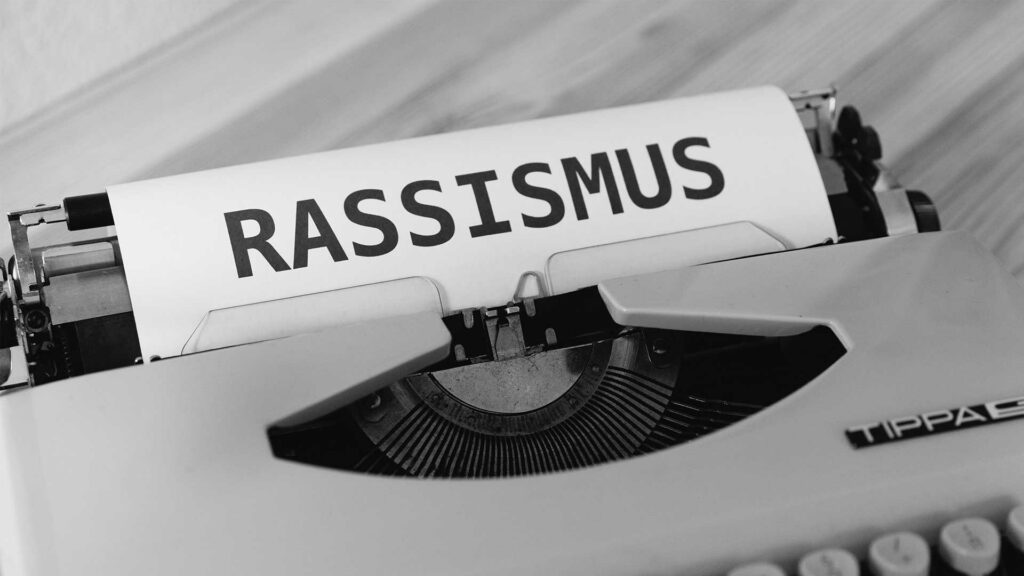 Auf einem Blatt, das in eine Schreibmaschine gespannt ist, steht in Großbuchstaben das Wort Rassismus. Das Bild ist schwarz-weiß.