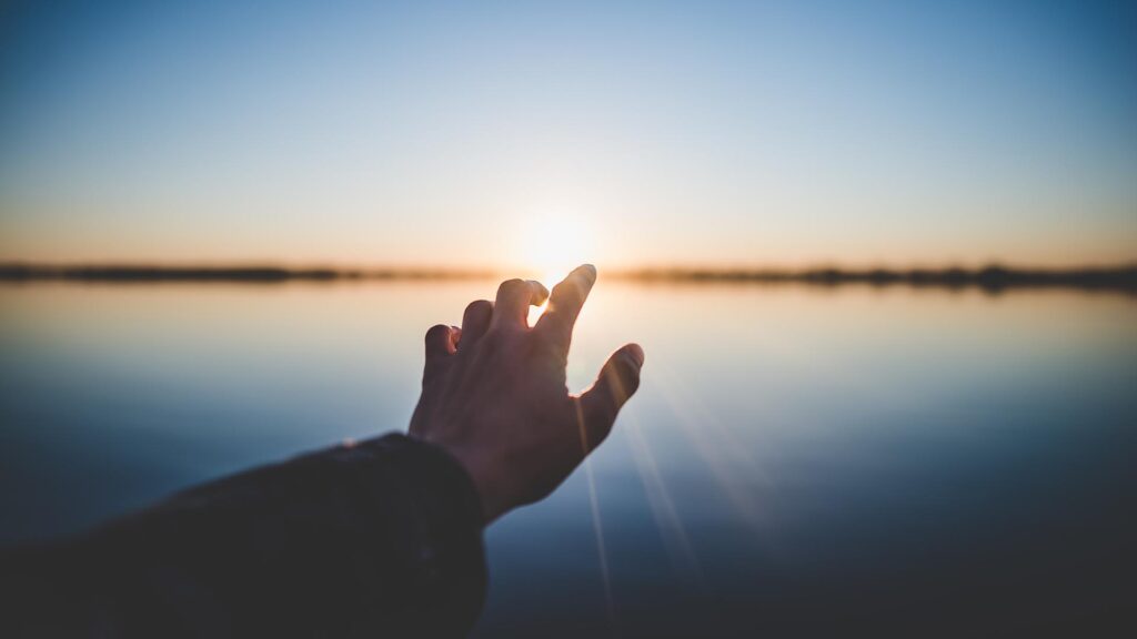 Hand fasst Richtung untergehender Sonne über See, poetisch