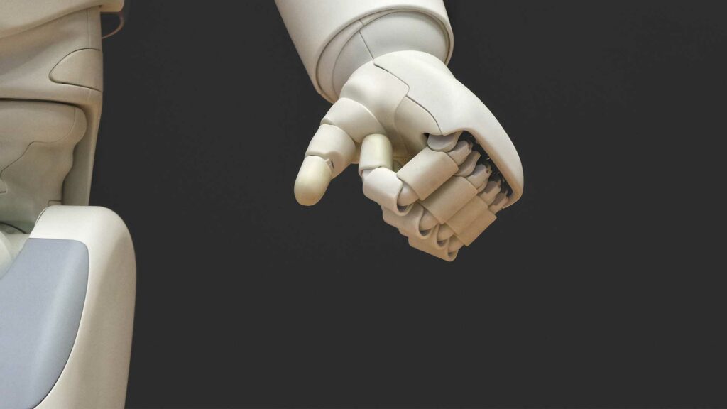 Zu sehen ist der Körper, bzw. die Hand eines Roboters vor dunklem Hintegrund