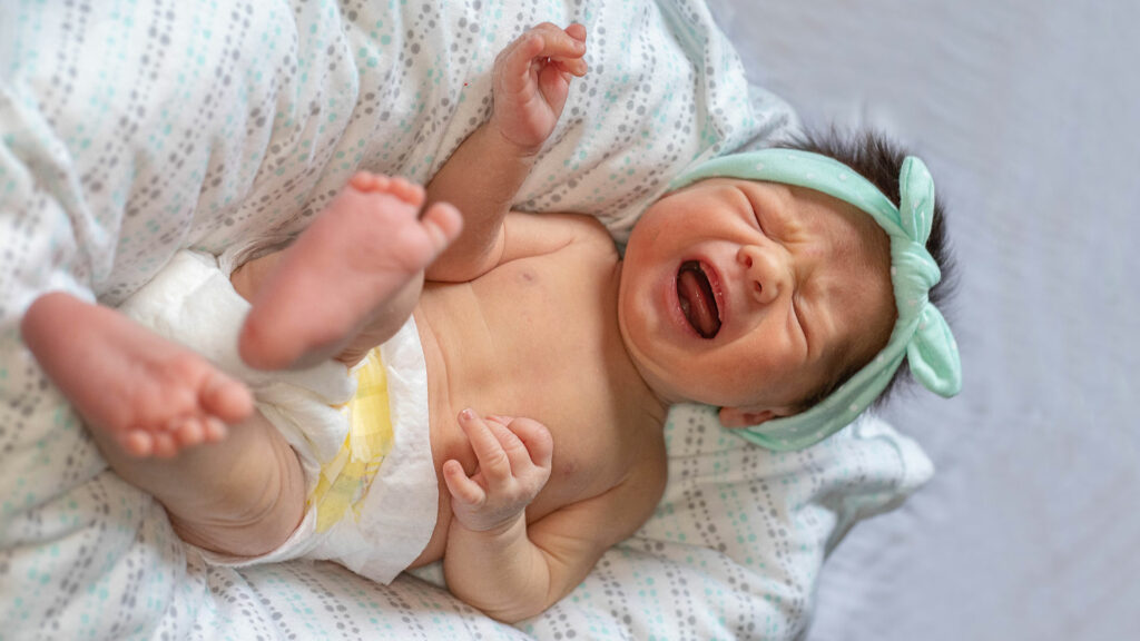 Ein Baby liegt auf dem Rücken und schreit.