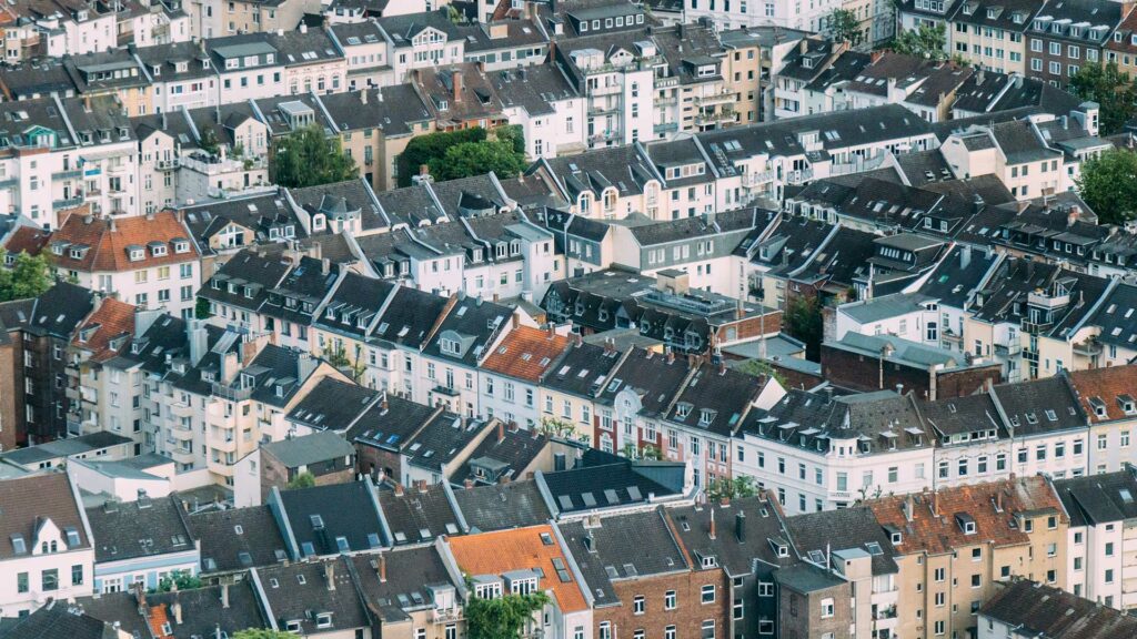 Dicht bebaute Stadtansicht mit vielen Altbauhäusern, deren Dächer schwarz, rot und grau gedeckt sind. Die Fassaden sind in verschiedenen Pastell- und Erdtönen gehalten, mit zahlreichen Fenstern und begrünten Innenhöfen.
