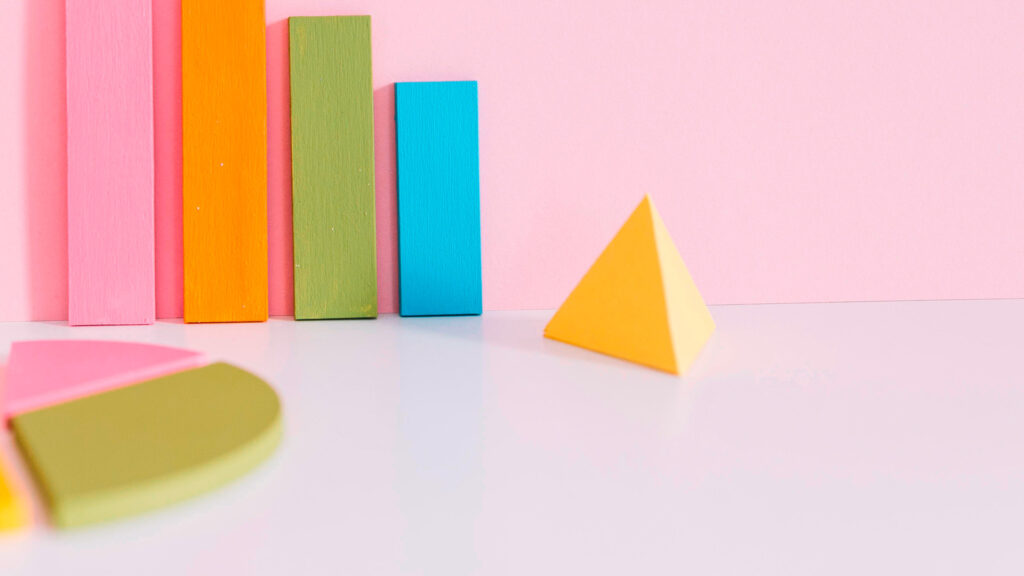 Bunte Holzformen als Balken- und Tortendiagramm vor rosa Hintergrund; Darstellung wirkt spielerisch und stilisiert.