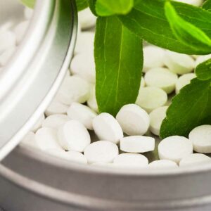 Blätter der Stevia-Pflanze und Stevia-Tabletten in kleiner Dose.