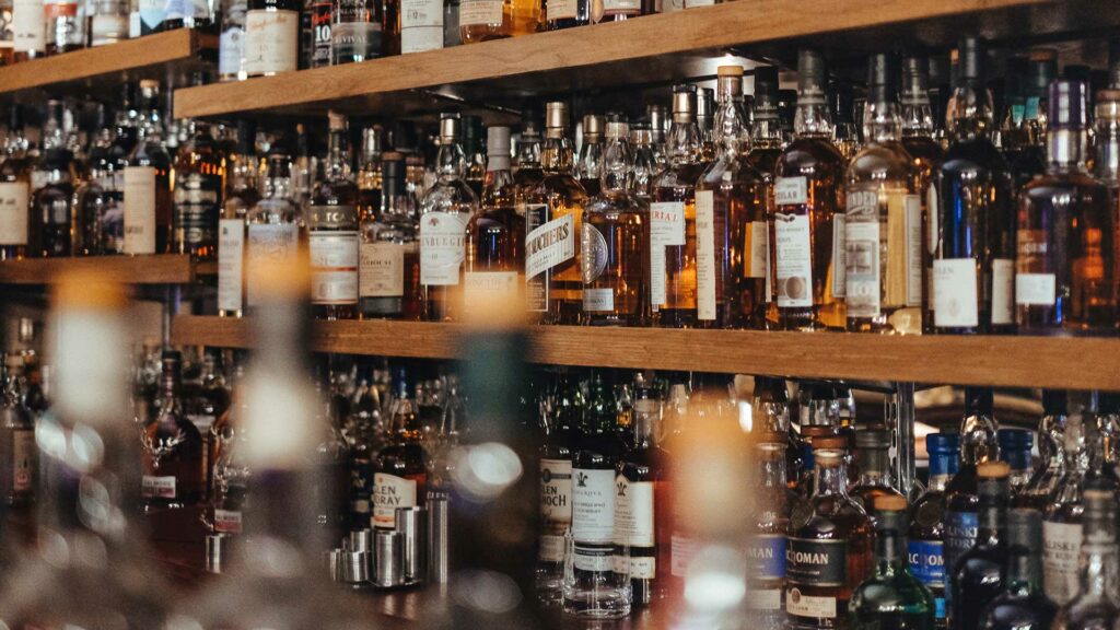 Eine Bar mit mehreren Holzregalen, gefüllt mit einer großen Auswahl an Whiskyflaschen in verschiedenen Formen und Farben.