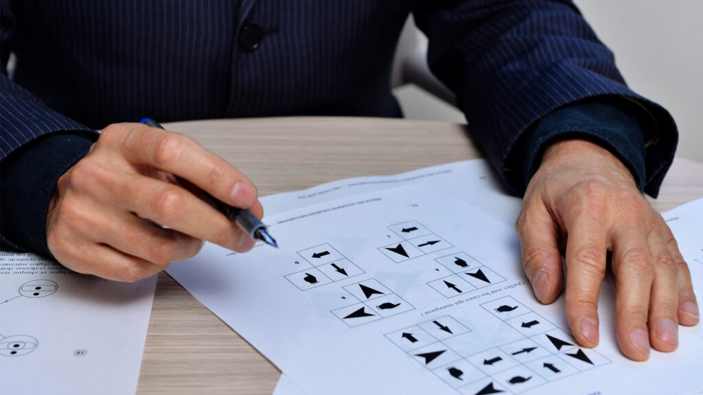 Ein Mann sitzt mit einem Stift in der Hand an einem Tisch und macht IQ-Test.