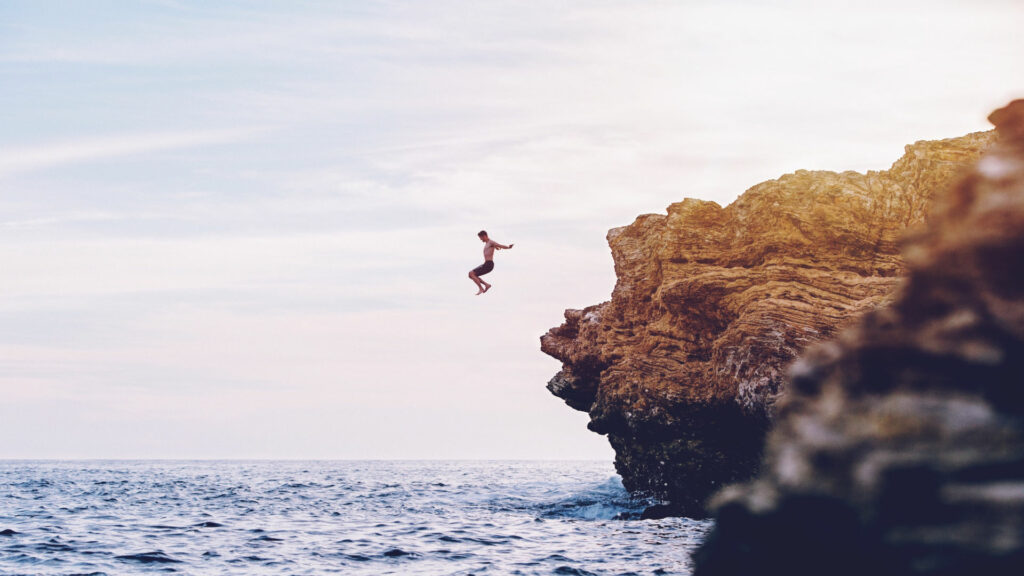 Mann springt von einer Klippe ins Meer