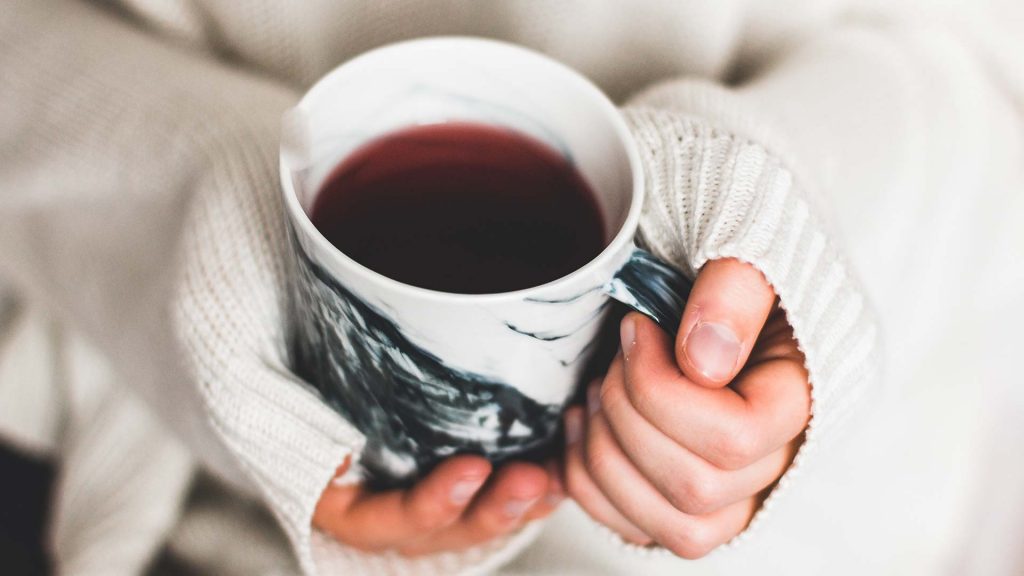 Frau hat einen dicken Pulli an und hält eine Teetasse