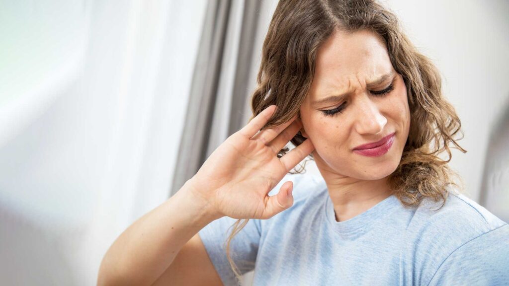 Frau hält sich das Ohr und den Kiefer wegen Tinnitus