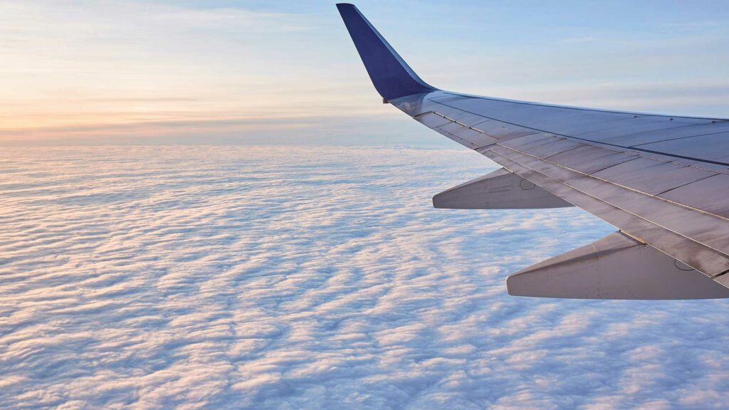 Zu sehen ist der Flügel eines Flugzeugs über einem Meer aus hellblauen Wolken.