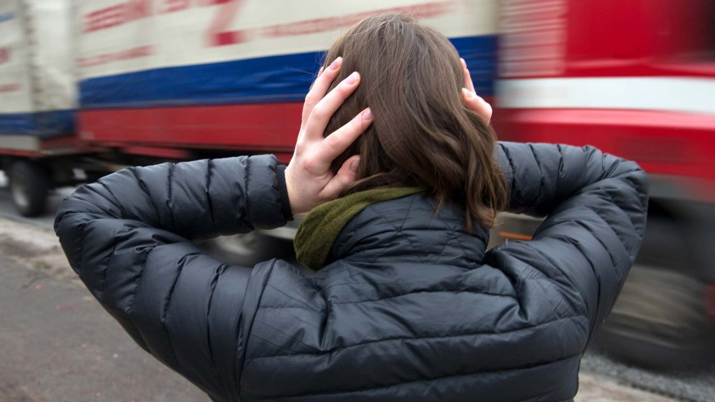 Eine Frau hält sich vor einem nahenden LKW die Ohren zu.