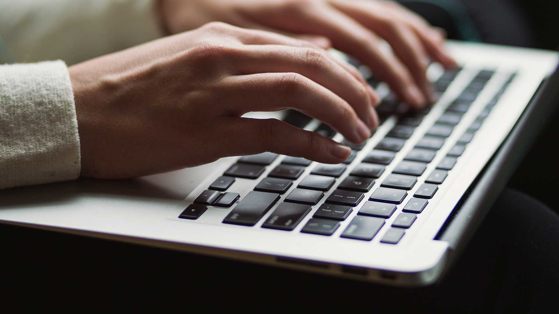 Die Finger einer Frau gleiten über die Tastatur eines Laptops.