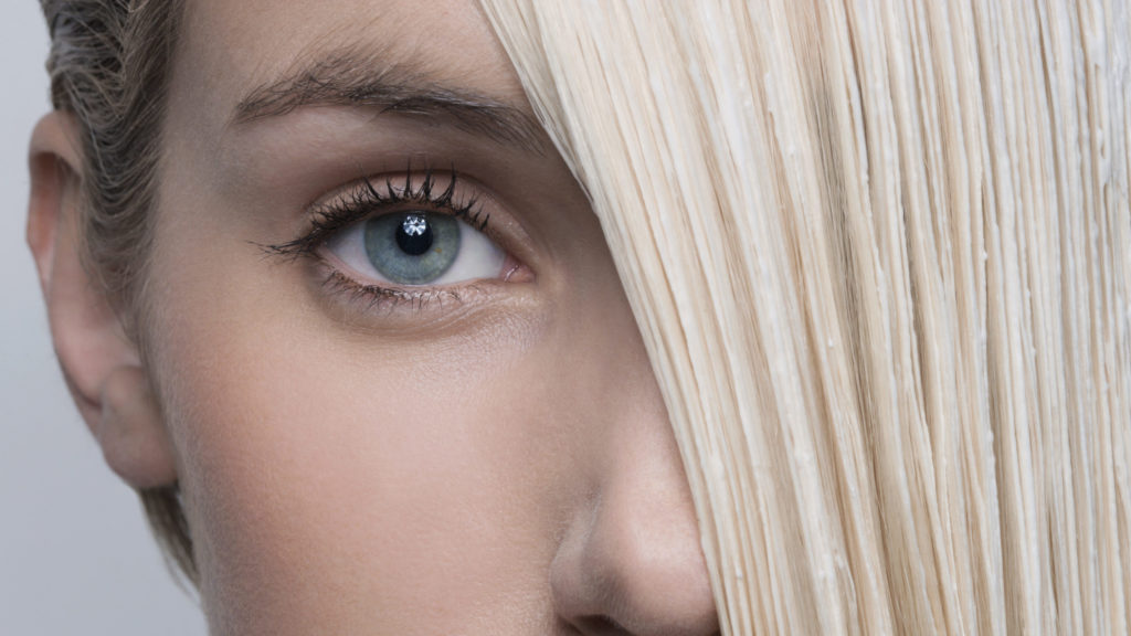 Junge Frau mit aufgetragener Blondierung im Haar.