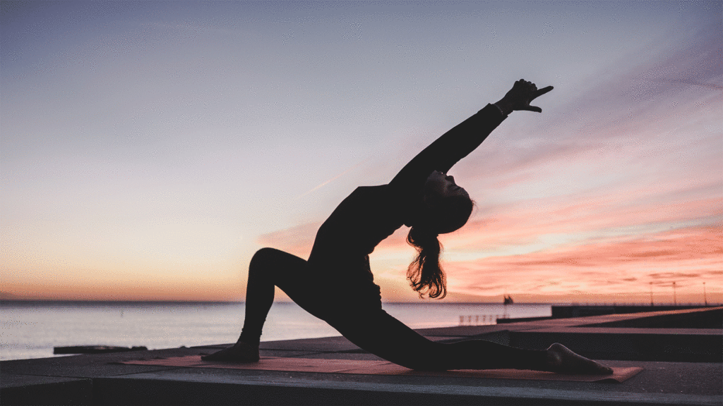 Eine Frau führt am Meer eine Yoga-Übung aus.