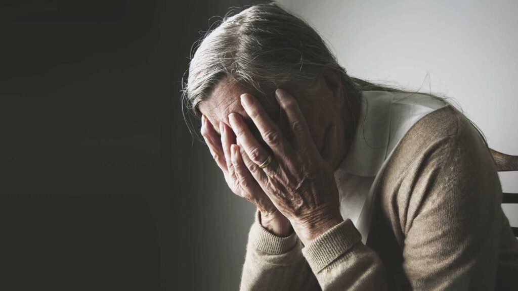 Alte Frau hält sich den Kopf