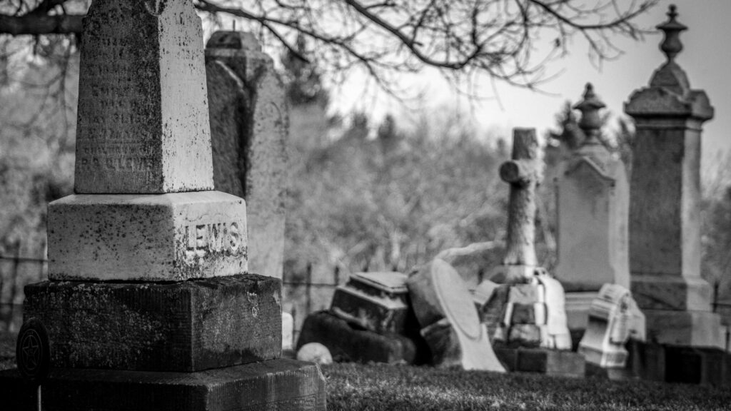 Eine Schwarzweißaufnahme von einem verlassenen Friedhof. Im Fokus steht ein Grabstein.
