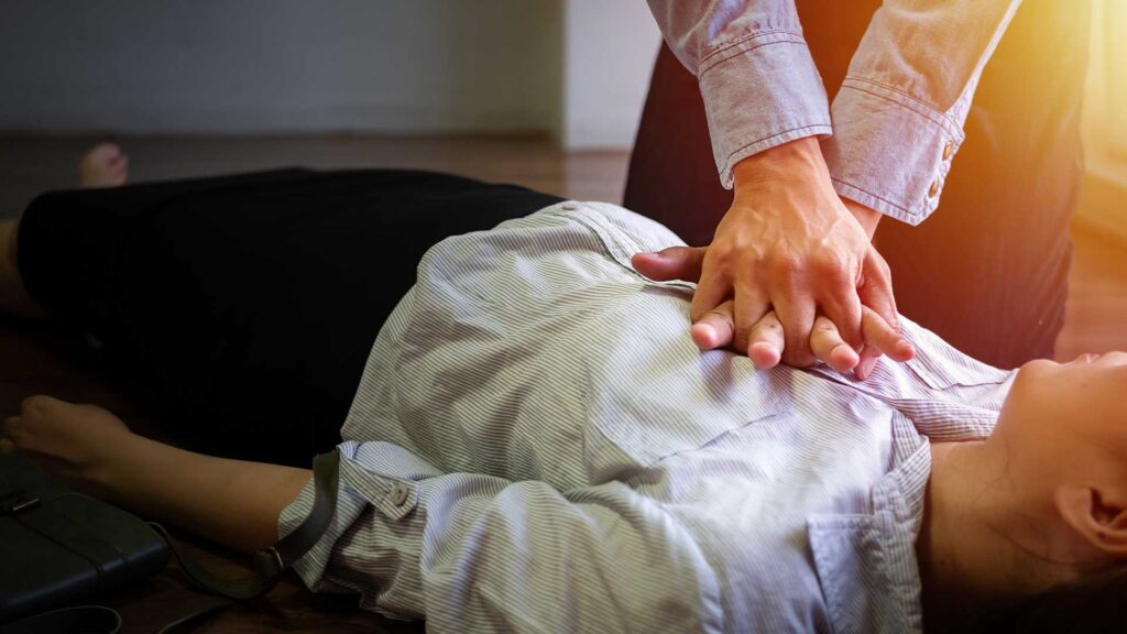Eine Person führt eine Herz-Druck-Massage an einer bewusstlosen Person durch, die auf dem Boden liegt.