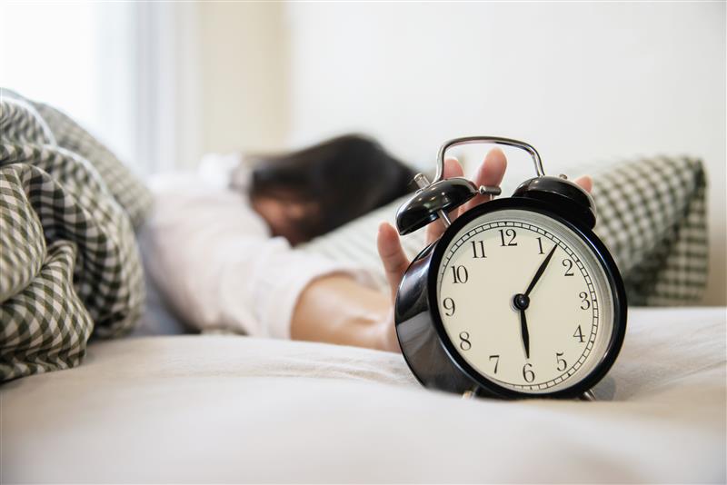 Eine Person liegt in ihrem Bett und greift zum Wecker.