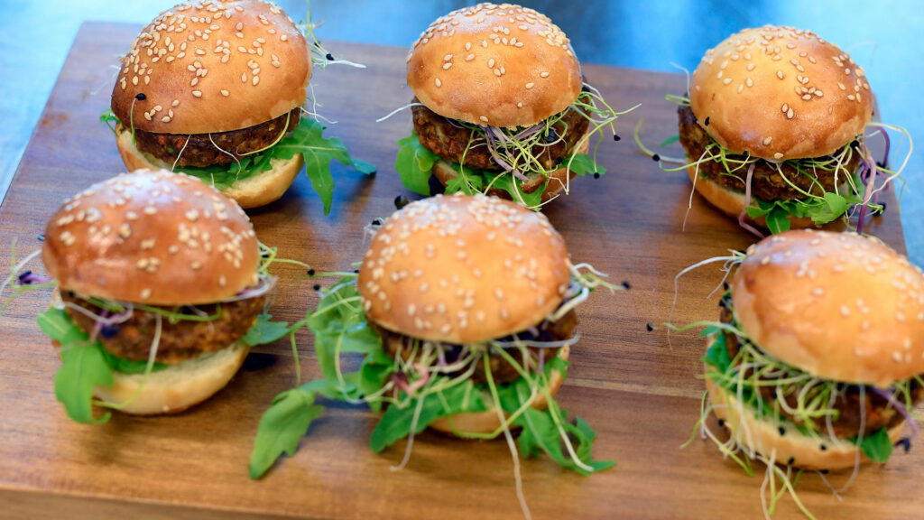 Abgebildet sind sechs Mini-Burger auf einer Holzplatte.