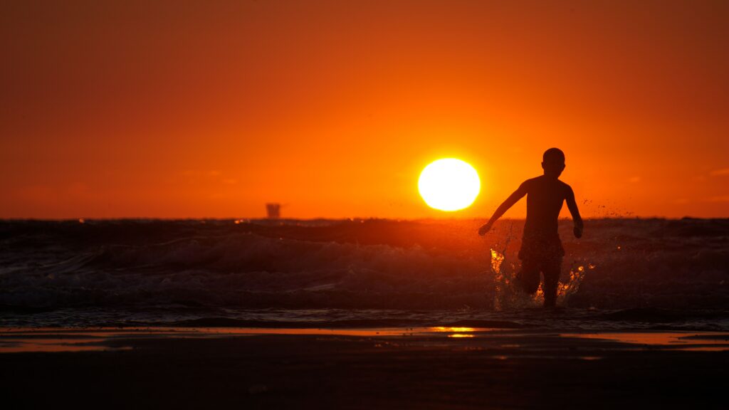 Ein Kind läuft vor einem Sonnenuntergang ins Meer.