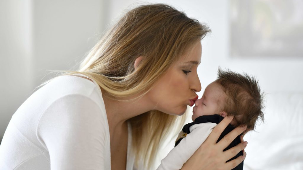 Mutter küsst ihr neugeborenes Baby auf die Nase und hält es in ihren Händen.