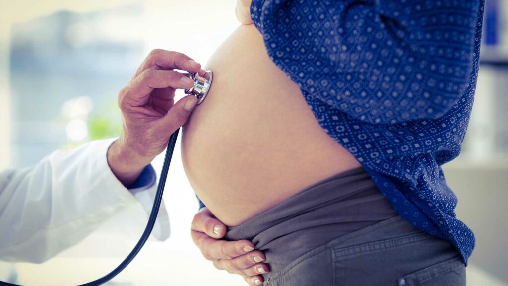 Bauch einer schwangeren Frau wird von einem Arzt mit einem Stethoskop abgehört.