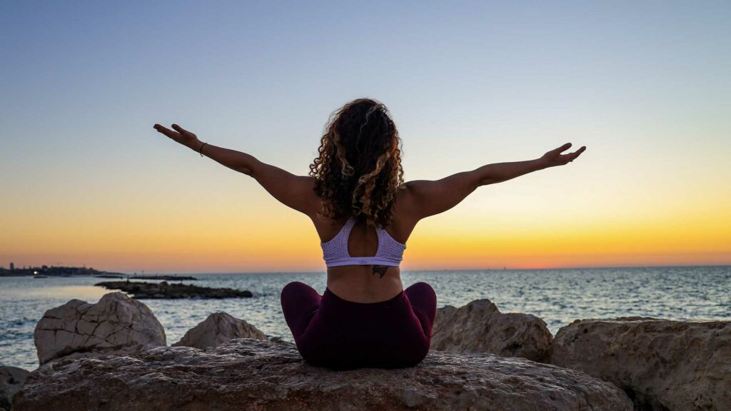 Junge Frau in Yoga-Pose von hinten vor Sonnenuntergang.